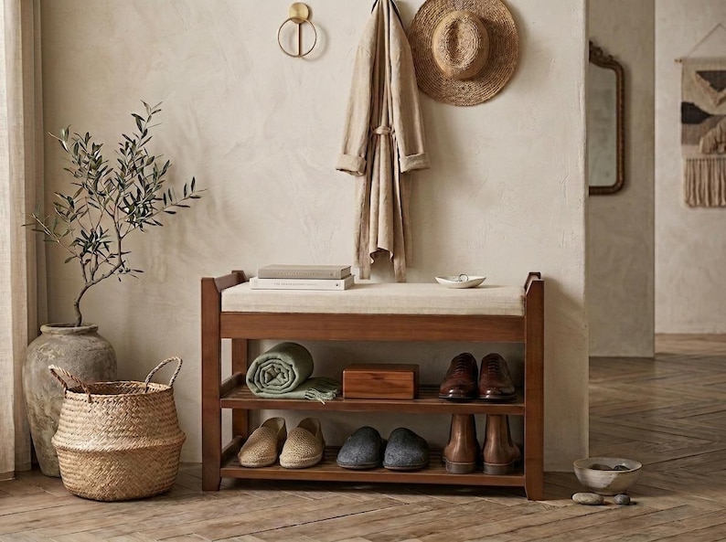 Peut inclure: Un banc &agrave; chaussures rectangulaire en bois dot&eacute; d'un coussin d'assise beige et de deux &eacute;tag&egrave;res de rangement ouvertes. Les &eacute;tag&egrave;res contiennent une couverture verte roul&eacute;e, une bo&icirc;te en bois et plusieurs paires de chaussures.