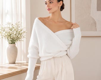 May include: A white long-sleeve sweater featuring a deep V-neckline with a wrap-style front, drop shoulders, and ribbed cuffs. The sweater is paired with light beige trousers that have a high-waisted fit and a clean, tailored appearance.