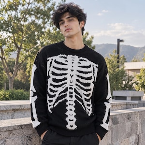 Könnte beinhalten: Ein schwarzer Langarmpullover mit einer großen, weißen, gestrickten Skelett-Brustkorb-Grafik auf der Vorderseite, die sich bis über die Ärmel erstreckt. Das Kleidungsstück hat einen Rundhalsausschnitt sowie gerippte Bündchen und Saum.