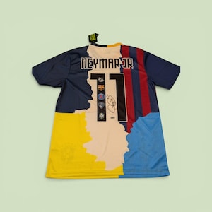 Pode incluir: Uma camisa de futebol Neymar Jr. com um design de blocos de cores. A camisa apresenta o número 11, o nome "NEYMAR JR" nos ombros e logotipos de equipes. A camisa tem um esquema de cores azul marinho, amarelo, vermelho e azul claro.