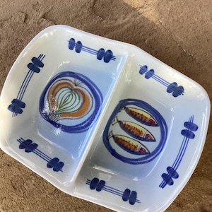 May include: A rectangular white ceramic divided serving dish with rounded corners. The dish features hand-painted blue line accents and two central illustrations: one of a single onion and one of three small fish, rendered in blue, orange, and green.