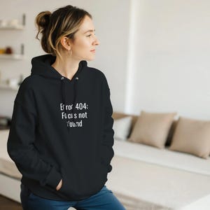 May include: A black hooded sweatshirt featuring the white text "Error 404: Focus not found". The hoodie has a drawstring and a front pocket. The person is wearing the hoodie.