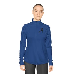Puede incluir: Una camiseta deportiva azul real de manga larga con cuello con cremallera de un cuarto. Una silueta negra de un corredor está en el pecho izquierdo. La parte superior está hecha de un material ligero y transpirable.