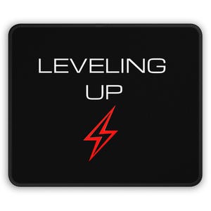 Puede incluir: Alfombrilla de ratón rectangular negra con las palabras blancas "LEVELING UP" y un rayo rojo. La alfombrilla tiene un borde negro.