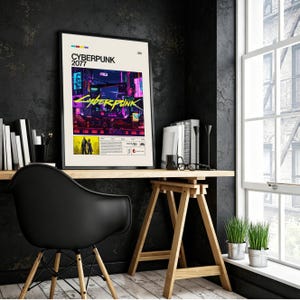 May include: A framed poster featuring the text "CYBERPUNK 2077" in a bold, modern font. The artwork showcases a vibrant, neon-lit cityscape with a futuristic aesthetic. The poster is displayed on a wooden desk with a black chair.