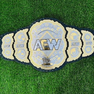 Op de afbeelding: Een worstelkampioensriem met een zwarte leren band en een grote, sierlijke zilveren en gouden middenplaat. De middenplaat bevat de letters "AEW" en de woorden "WORLD CHAMPION". De riem heeft verschillende zijplaten met de letters "AEW" en wereldbolontwerpen.
