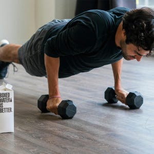 May include: A person doing push-ups with black dumbbells on a wooden floor. A white carton of boxed water is visible with the text "BOXED WATER IS BETTER."