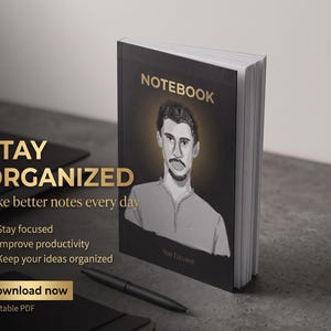 Può includere: Un taccuino nero con la scritta "NOTEBOOK" in oro. La copertina presenta un disegno del volto di un uomo. Sono visibili anche le scritte "STAY ORGANIZED" e "Take better notes every day". Il taccuino è su una superficie grigia.