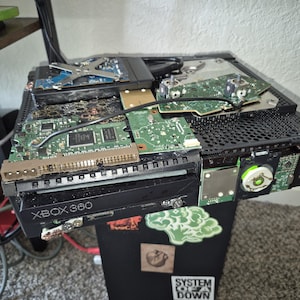 May include: A disassembled Xbox 360 console, revealing its internal components such as circuit boards and chips. The black casing is partially removed, exposing the intricate electronics. A USB drive is inserted. The text "XBOX 360" is visible on the console's front.