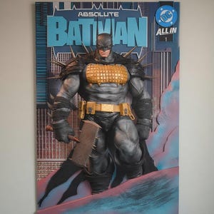 May include: A 3D wall art piece featuring the Absolute Batman comic book cover. The figure wears a grey suit with a gold grid chest plate, spiked shoulder armor, and a gold utility belt. Batman holds a large, spiked axe against a city background.