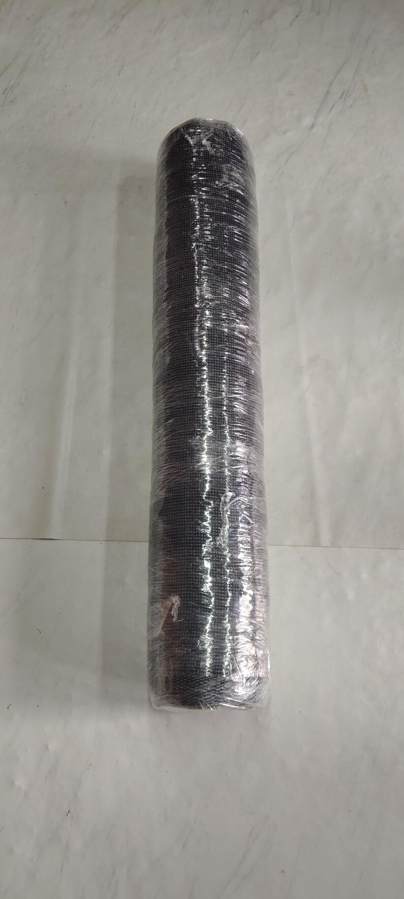 May include: A cylindrical roll of black mesh material tightly wrapped in clear plastic film. The mesh features a consistent grid pattern throughout its length, and the protective plastic covering creates a reflective, crinkled texture over the surface.