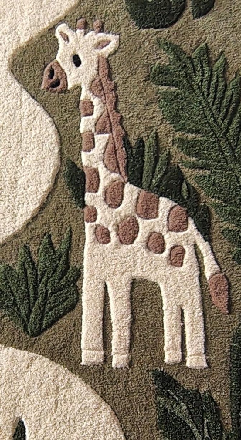 May include: A tufted textile wall hanging featuring a cream-colored giraffe with brown spots standing amidst dark green foliage and textured cream shapes. The design uses a punch needle technique to create a raised, tactile surface with distinct patterns.