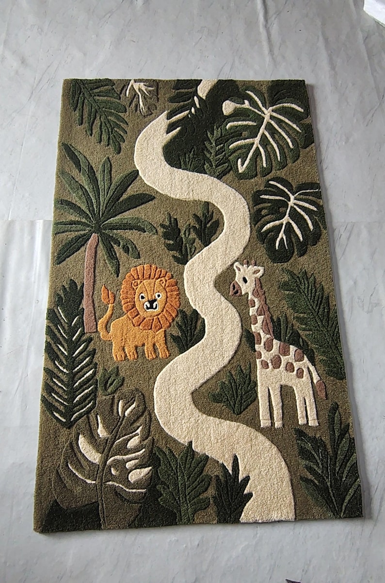 "Jungle safari themed tufted area rug featuring a lion, giraffe, tropical palm leaves, and a winding cream pathway. The rug is displayed in a children's playroom with wooden furniture, plants, and soft natural lighting, creating a cozy nursery and playroom decor setting."