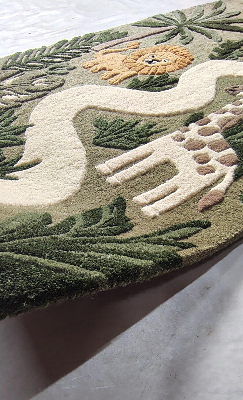 May include: A rectangular tufted rug featuring a jungle theme with a light green background. The design includes a tan lion, a white winding path, and a giraffe with brown spots. Dark green palm leaves and foliage are tufted throughout the rug.