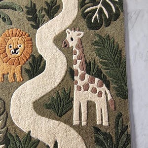 May include: A tufted rug featuring a jungle scene with a winding white path, a brown lion with a textured mane, and a white giraffe with brown spots. The background is olive green with various dark green tropical leaf patterns throughout.
