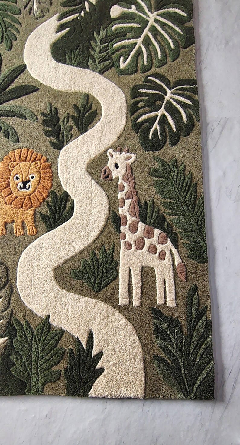 May include: A tufted rug featuring a jungle scene with a winding white path, a brown lion with a textured mane, and a white giraffe with brown spots. The background is olive green with various dark green tropical leaf patterns throughout.