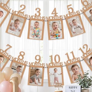 Puede incluir: Una guirnalda de fotos de hitos mensuales con doce marcos de cartulina dorada numerados del uno al doce con la palabra MONTHS, cada uno con una foto de bebé. Un globo dorado con el número uno y un pastel pequeño están sobre la mesa.