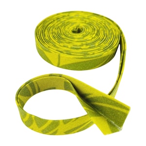 May include: A roll of bias tape featuring a vibrant yellow and green leaf pattern. The fabric trim is coiled into a circular shape with one end extending outward, displaying a folded edge design suitable for sewing and textile projects.