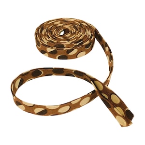 May include: A coiled length of brown fabric bias tape featuring a repeating pattern of tan and dark brown circular dots. The tape is folded along its length, showing a consistent width and a smooth, flat texture throughout the entire coiled strip.