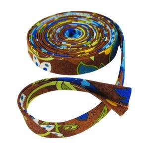 May include: A roll of double fold bias tape featuring a brown background with a repeating floral pattern in shades of blue, lime green, and white. The fabric strip is coiled into a tight circle with one end extending outward to show the folded edges.