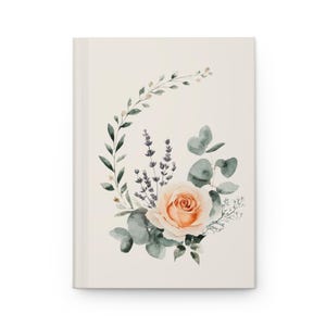 May include: A cream-colored journal with a watercolor floral design. The design features a peach rose, lavender, and eucalyptus leaves arranged in a circular pattern. The journal has a clean, minimalist aesthetic.