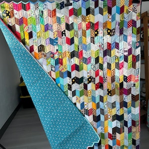 May include: A handmade quilt with a vibrant patchwork design. The quilt features a geometric pattern of colorful fabric pieces in various colors and patterns. The reverse side is a teal fabric with a white floral pattern. The quilt is approximately 70 inches by 80 inches.