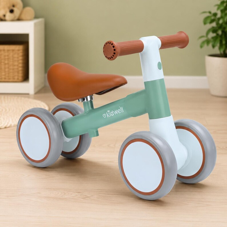 May include: A four-wheeled balance bike for toddlers featuring a sage green frame with the Kidwell logo, a brown seat, brown handlebars, and light blue wheel hubs with grey tires. The design includes a white steering column and frame accents.