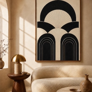 May include: A framed abstract art print with a black and cream geometric design. The artwork features arch shapes and lines. The room also includes a gold lamp, a wooden side table, a beige sofa, and a round coffee table.