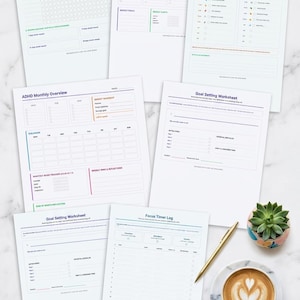 Può includere: Una raccolta di pagine di pianificazione stampabili, tra cui un tracker delle abitudini di 30 giorni, un pianificatore settimanale ADHD e fogli di lavoro per la definizione degli obiettivi. Sono presenti anche una penna d'oro, una tazza di caffè con latte art e una piccola pianta succulenta.