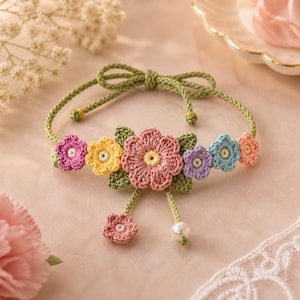 Può includere: Un braccialetto all'uncinetto fatto a mano con un design floreale. Il braccialetto ha un cordoncino verde con chiusura a fiocco. I fiori sono nelle tonalità di rosa, giallo, viola e blu, con foglie verdi. Un piccolo fiore rosa e una perla pendono dal centro.