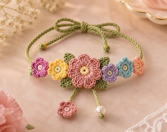 May include: A handmade crochet bracelet featuring a floral design. The bracelet has a green cord with a bow closure. The flowers are in shades of pink, yellow, purple, and blue, with green leaves. A small pink flower and a pearl dangle from the center.