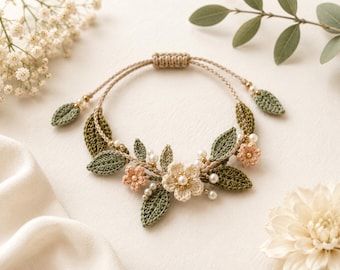 May include: A handmade crochet bracelet featuring a floral design. The bracelet has a tan cord with olive green leaves, peach and cream flowers, and small pearl accents. The adjustable closure is a braided tan cord.