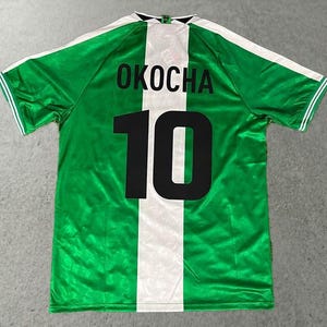 May include: Green and white soccer jersey with the name "OKOCHA" and the number "10" in black. The jersey has a white vertical stripe down the back and white accents on the sleeves.