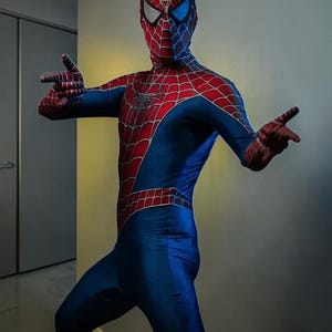 May include: A full-body Spiderman costume featuring a vibrant red and blue colour scheme with a black web pattern printed across the chest, arms, and mask. The mask includes large, white, triangular eye lenses with a thin black border outline.