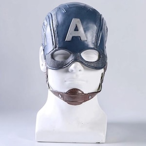 Puede incluir: Una máscara azul oscuro de Capitán América con una letra A plateada en la frente, aberturas para los ojos texturizadas y una correa de barbilla marrón con remaches metálicos, sobre un busto de maniquí blanco.