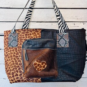 May include: A large tote bag with a patchwork design. The bag features panels of leopard print, black crocodile-textured leather, and brown fur with a leopard print heart. Zebra print straps and snake print accents add to the unique style.