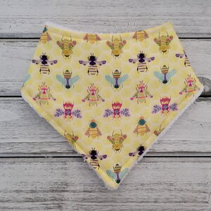 May include: A yellow bandana with a pattern of colorful bees and honeycomb. The bandana is made of soft fabric and has a white fleece lining.