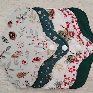 May include: Five reusable cloth menstrual pads with snap closures. The pads feature various nature-themed patterns, including mushrooms, berries, and pinecones, in shades of white, green, and red. The pads are designed for comfort and eco-friendliness.