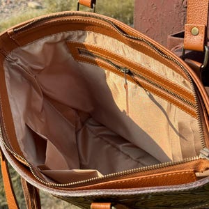 Pode incluir: Vista aberta de uma bolsa tote de couro marrom com fecho de z&iacute;per. A bolsa tem um interior marrom claro com v&aacute;rios bolsos. O exterior apresenta um padr&atilde;o em relevo e al&ccedil;as de couro. A bolsa tem um tema western.