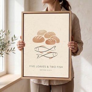 May include: A framed art print featuring a beige background with illustrations of bread loaves and two fish. The text "FIVE LOAVES & TWO FISH" and "MATTHEW 14:13-21" are printed below the illustrations. The frame is a light brown color.