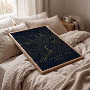 Può includere: Una stampa di mappa incorniciata della città di Westminster, Regno Unito. La mappa presenta linee dorate su sfondo blu scuro. La cornice è in legno chiaro. Il testo "CITY OF WESTMINSTER UNITED KINGDOM" è visibile.