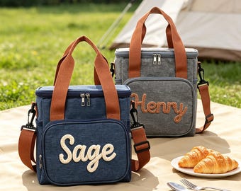 Könnte beinhalten: Zwei rechteckige isolierte Kühltaschen mit braunen Stoffgriffen und abnehmbaren Schultergurten. Eine Tasche ist marineblau mit dem in Weiß gestickten Namen Sage, die andere ist grau mit dem in Braun gestickten Namen Henry.