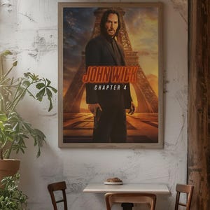Puede incluir: Póster enmarcado de la película "John Wick: Capítulo 4" con un hombre con traje sosteniendo un arma, con la Torre Eiffel de fondo. El título es naranja y el póster se exhibe en un ambiente de cafetería.
