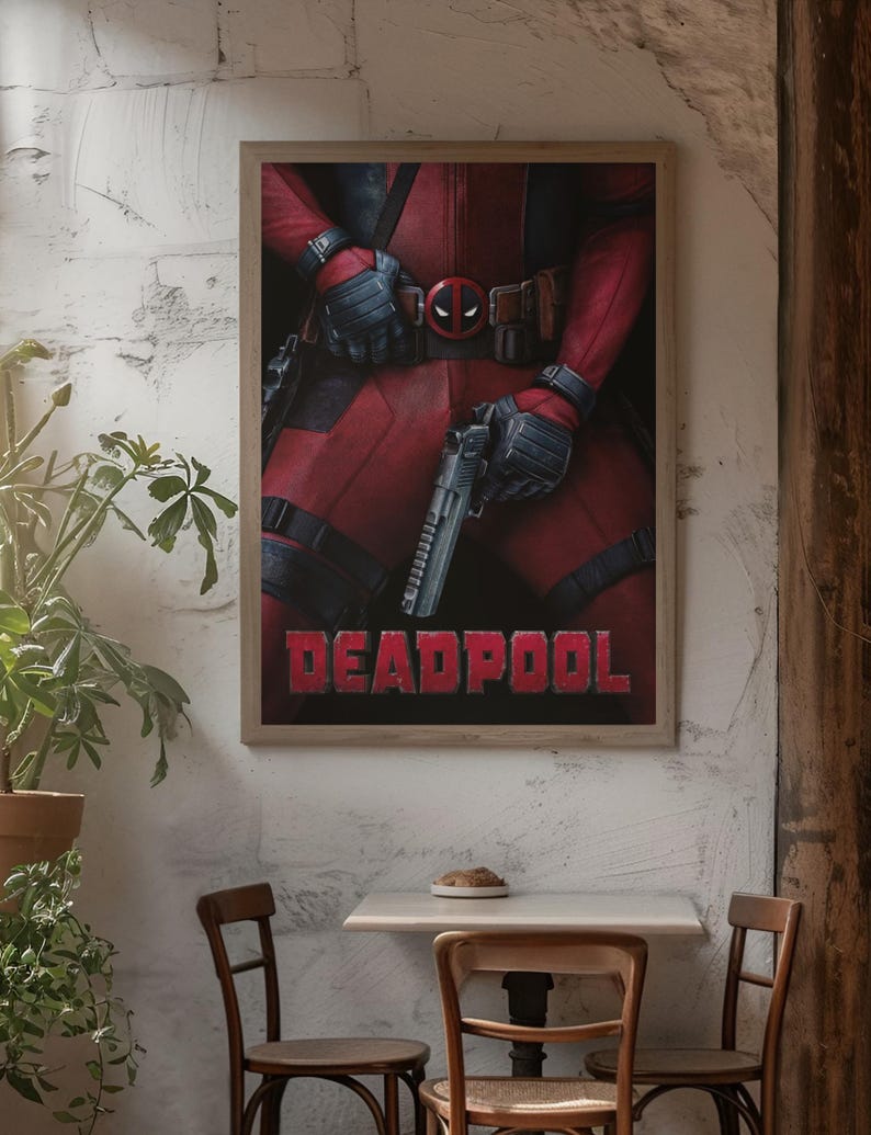 Puede incluir: P&oacute;ster enmarcado con Deadpool en un traje rojo y negro, sosteniendo una pistola. El p&oacute;ster tiene la palabra "DEADPOOL" en letras rojas. La imagen se muestra en un caf&eacute; con sillas de madera y una mesa peque&ntilde;a.