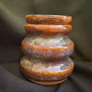 May include: A handcrafted ceramic vase with a unique, layered design. The vase features a rich color palette of brown, orange, and hints of blue and green. The glossy finish enhances the visual appeal of this decorative piece, perfect for home decor.