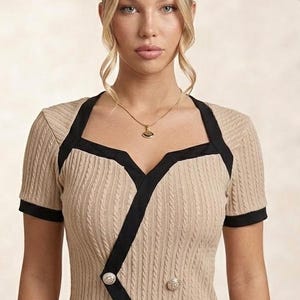Peut inclure: Un haut beige à manches courtes avec une texture en tricot torsadé vertical, doté d'un liseré noir le long de l'encolure carrée et d'un chevauchement diagonal sur le devant. Le vêtement comprend deux boutons argentés décoratifs et un pantalon blanc.