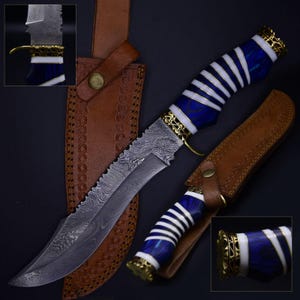 Puede incluir: Cuchillo de caza de acero de Damasco con una hoja dentada y un mango con detalles azules, blancos y dorados. El cuchillo viene con una funda de cuero marrón. El mango mide aproximadamente 12 cm de largo.