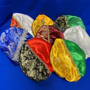 May include: A collection of satin bonnets in various colors, including white, blue, red, yellow, and green. Some bonnets feature paisley patterns and decorative trim. The bonnets are displayed on a blue surface.