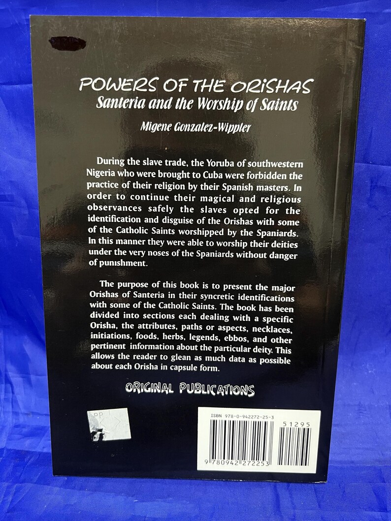 May include: A book titled "POWERS OF THE ORISHAS Santeria and the Worship of Saints" by Migene Gonzalez-Wippler. The book's cover is dark with white text. The text describes the history of Santeria and its syncretic relationship with Catholicism.