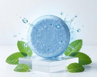 May include: A round, light blue solid shampoo bar with a textured surface, surrounded by splashing water droplets and vibrant green mint leaves. The circular bar is positioned on a clear, square acrylic block against a bright background.